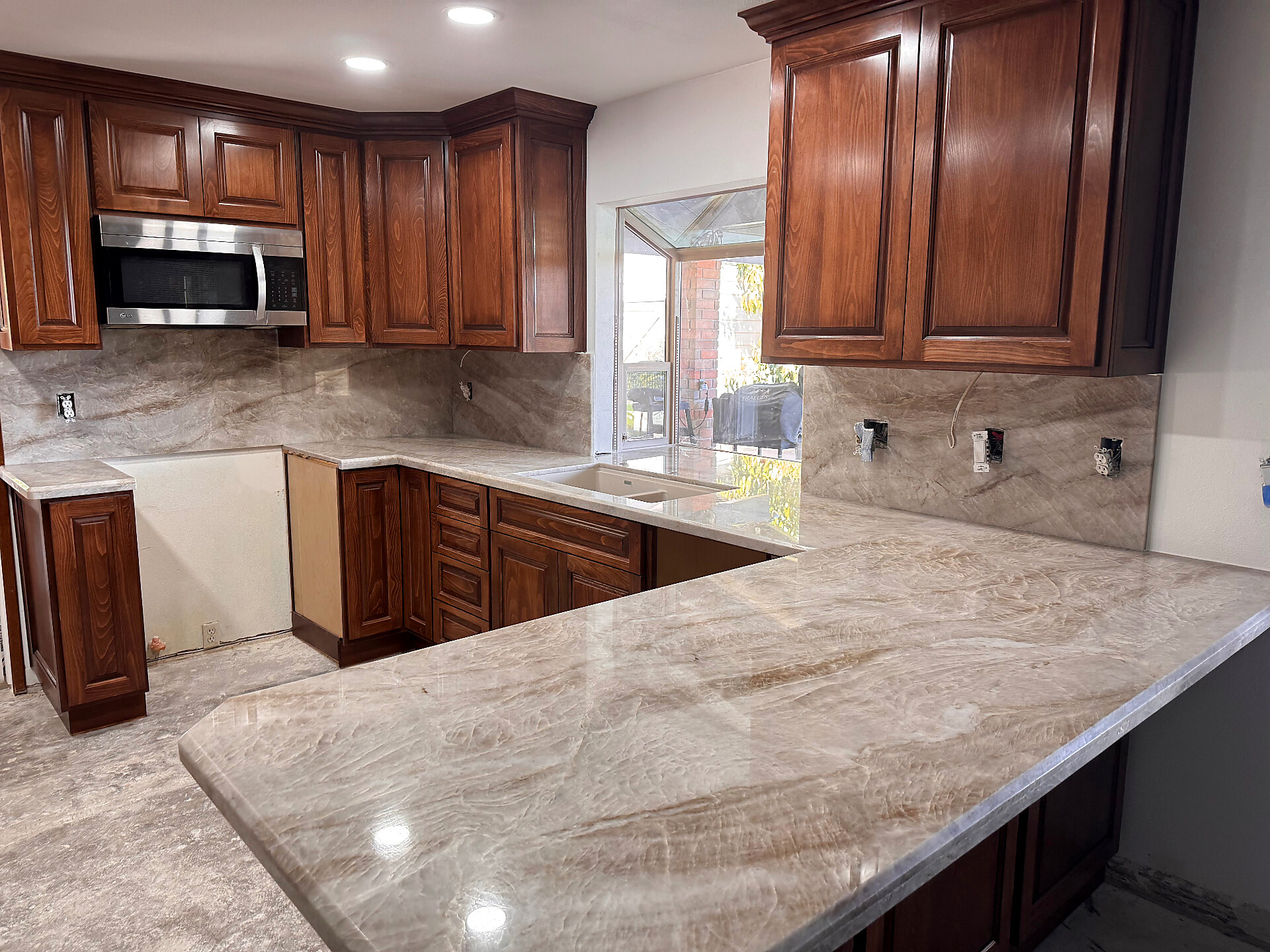 Warm-toned stone kitchen island with rich wood cabinetry and full-height backsplash